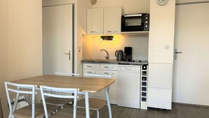 Une petite cuisine équipée d’un four à micro-ondes, d’une machine à café et d’un lave-vaisselle. On y trouve également une petite table à manger avec des chaises.