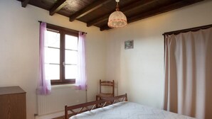 A bedroom with a wooden bed, a chair, a window with curtains, and a radiator. - 65 sqm cottage with fireplace, terrace, and children's play area (Saint-Médard-en-Forez)