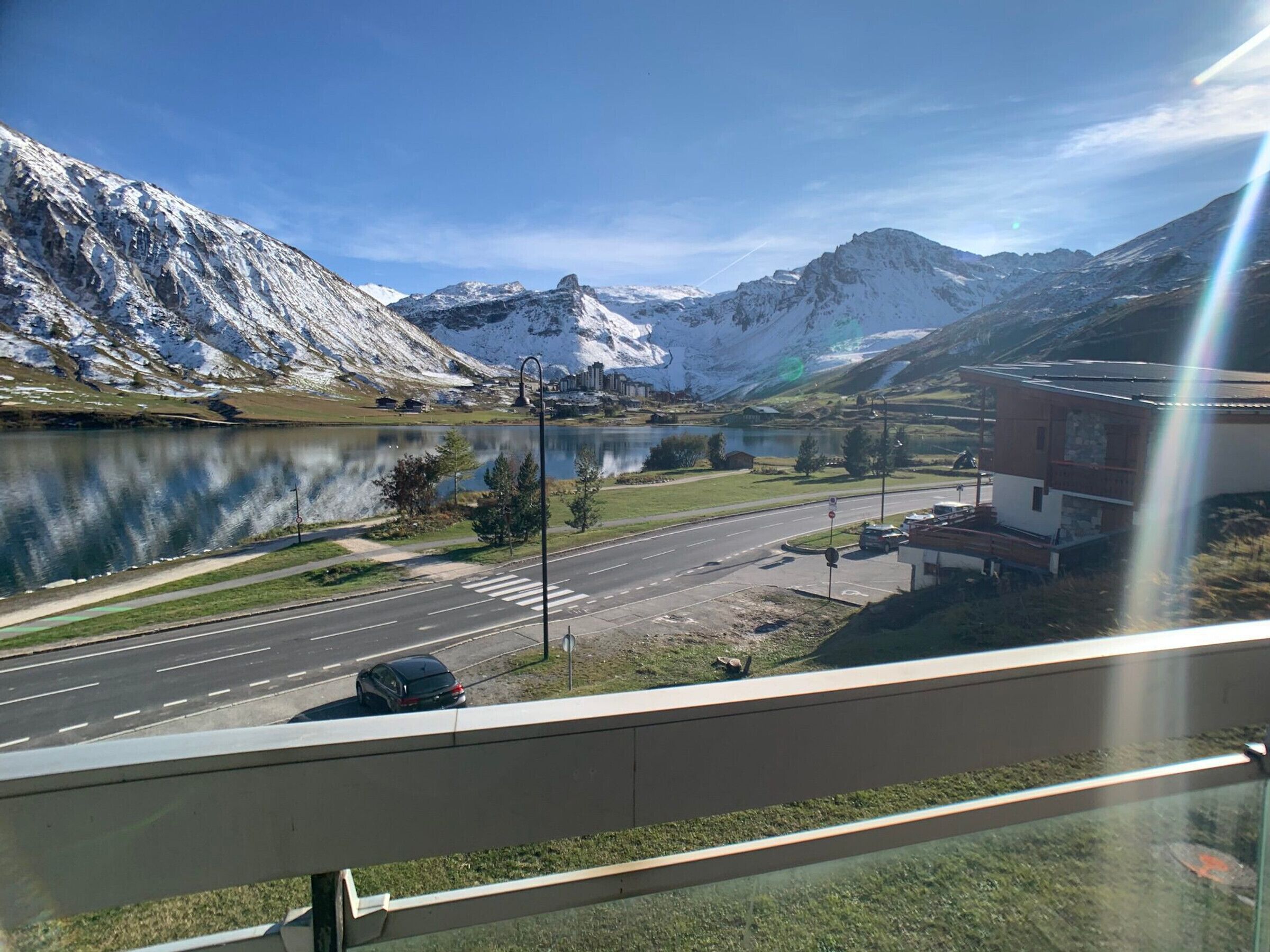 Une vue sur un lac, avec des montagnes en arrière-plan, une route où circulent des voitures et un bâtiment avec un toit rouge.