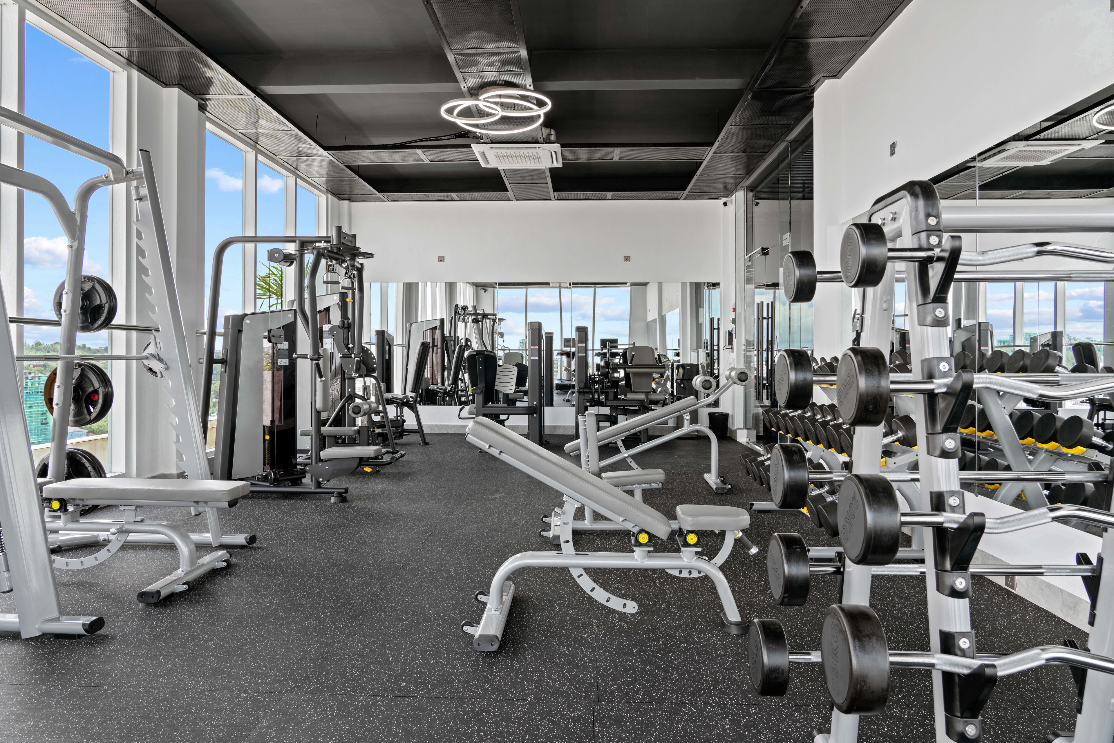 Un gimnasio con diversos equipos de ejercicio, amplias ventanas y un techo alto.