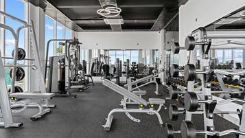 Un gimnasio con diversos equipos de ejercicio, amplias ventanas y un techo alto.