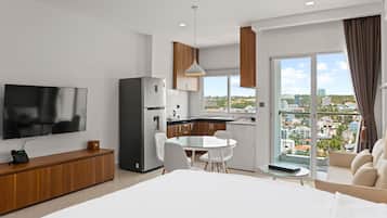 Une chambre d’hôtel moderne dotée d’un grand lit, d’un coin repas avec une table en verre, d’une cuisine équipée d’un réfrigérateur et d’un téléviseur fixé au mur.