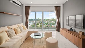 A modern living room with a sofa, glass coffee table, ottoman, and a flat-screen TV. - MLZ APARTMENTS (Sihanoukville)