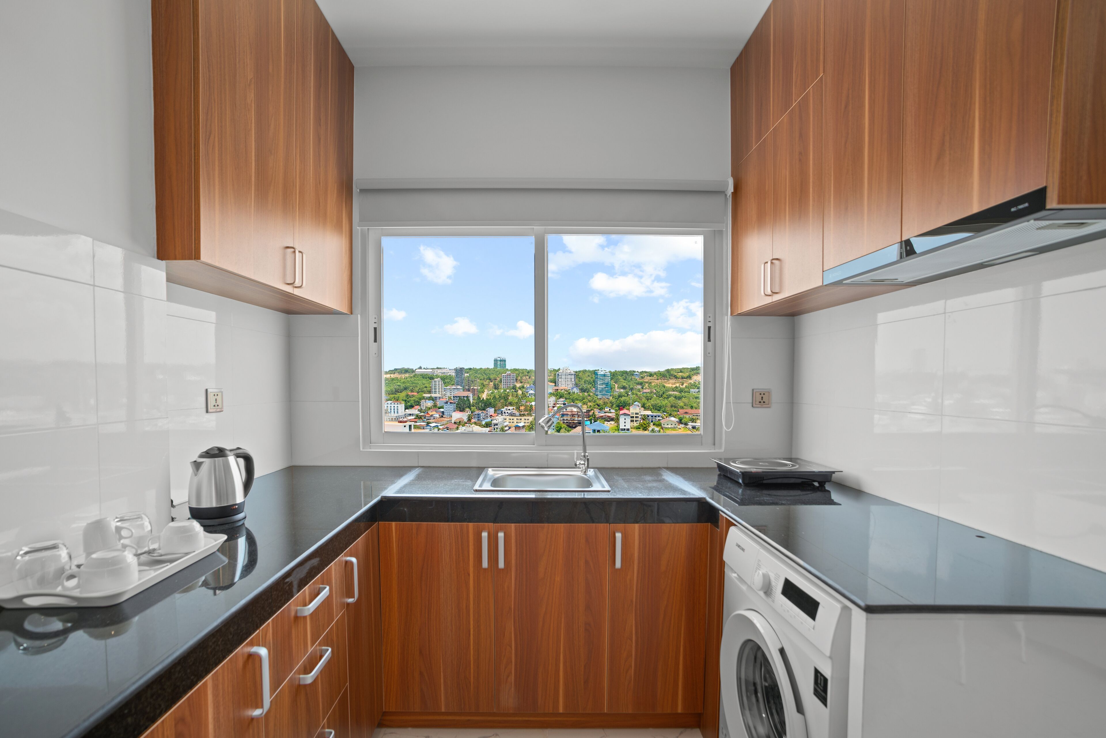 Eine moderne Küche mit Holzausstattung, einer integrierten Waschmaschine und einem großen Fenster mit Blick auf die Stadt.