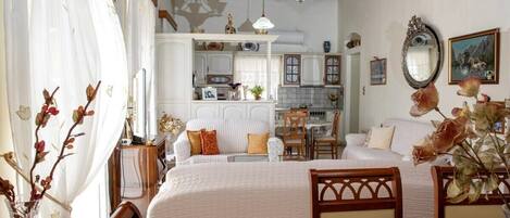 A cozy room with a wooden ceiling, a large bed, a dining table, and a kitchen in the background.