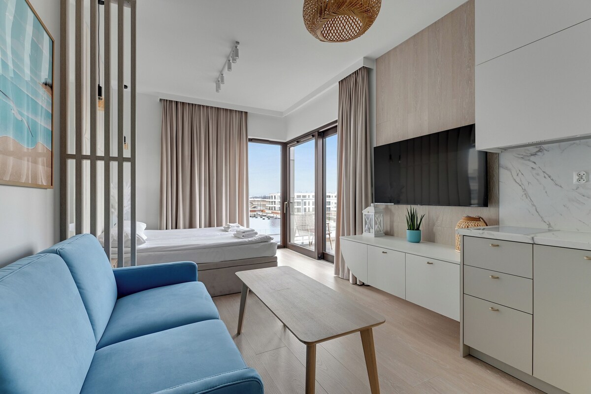 Une chambre d’hôtel moderne équipée d’un canapé, d’une petite table, d’un lit, d’une télévision et d’un coin cuisine.