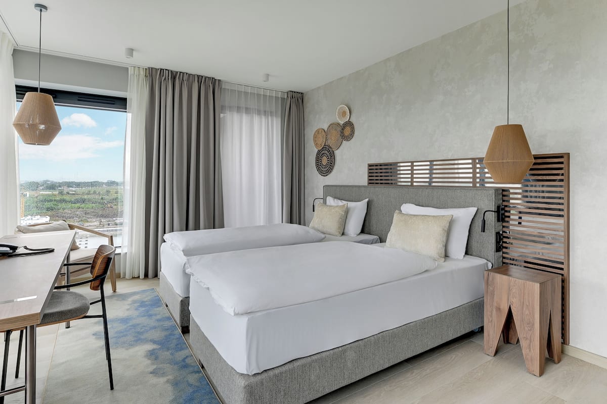 Una habitación de hotel moderna con dos camas, un escritorio y vistas a la ciudad.
