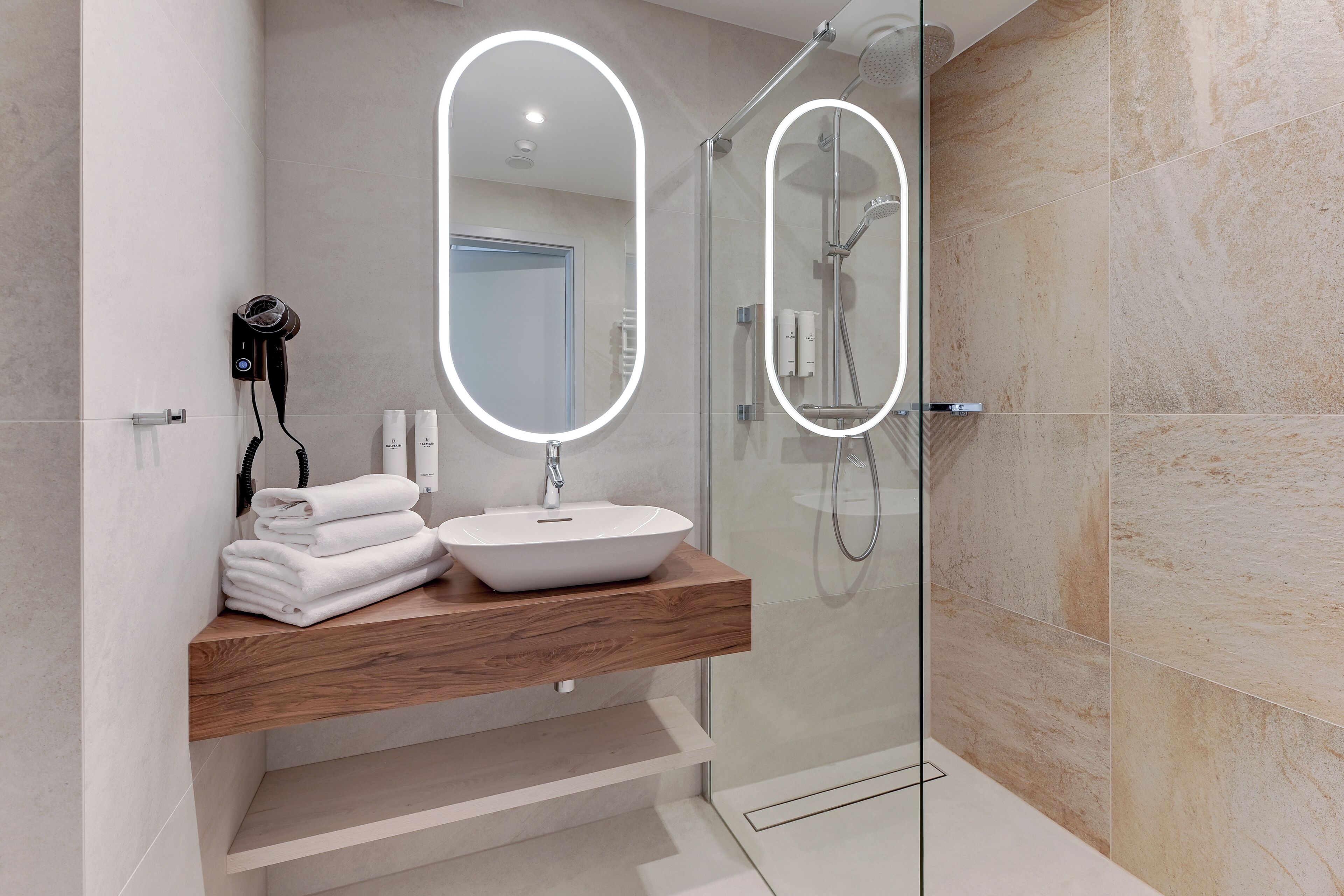 A modern bathroom with a wooden vanity, a white sink, and a glass-enclosed shower.