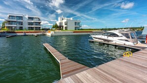 Een modern pand aan het water met een steiger, een witte boot en een gebouw met twee verdiepingen en balkons.