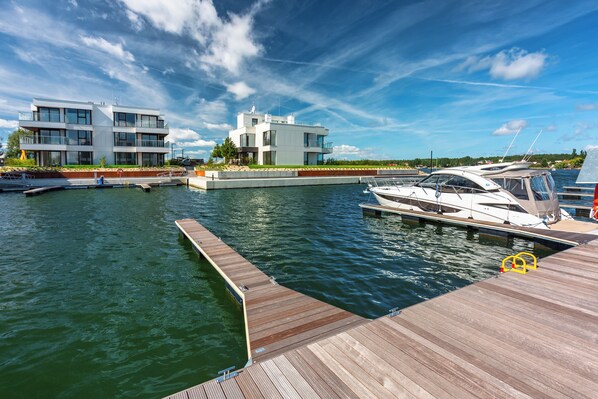 Une propriété moderne située au bord de l’eau, dotée d’un quai, d’un bateau blanc et d’un bâtiment à deux étages avec des balcons.