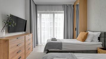 A modern bedroom with a bed, a TV, a wooden dresser, and a large window with curtains.