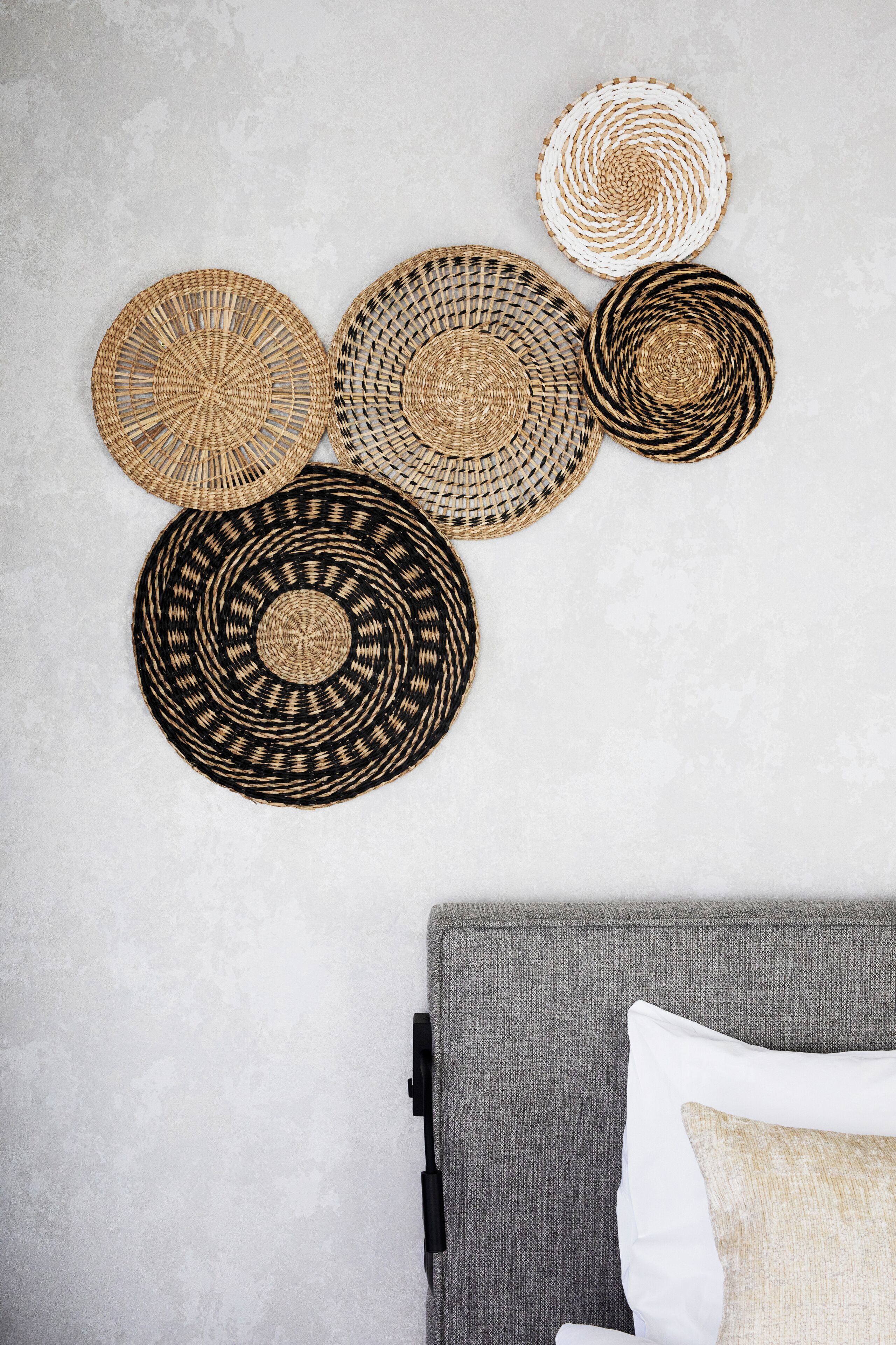 Un sofá gris con una almohada blanca frente a una pared con textura.