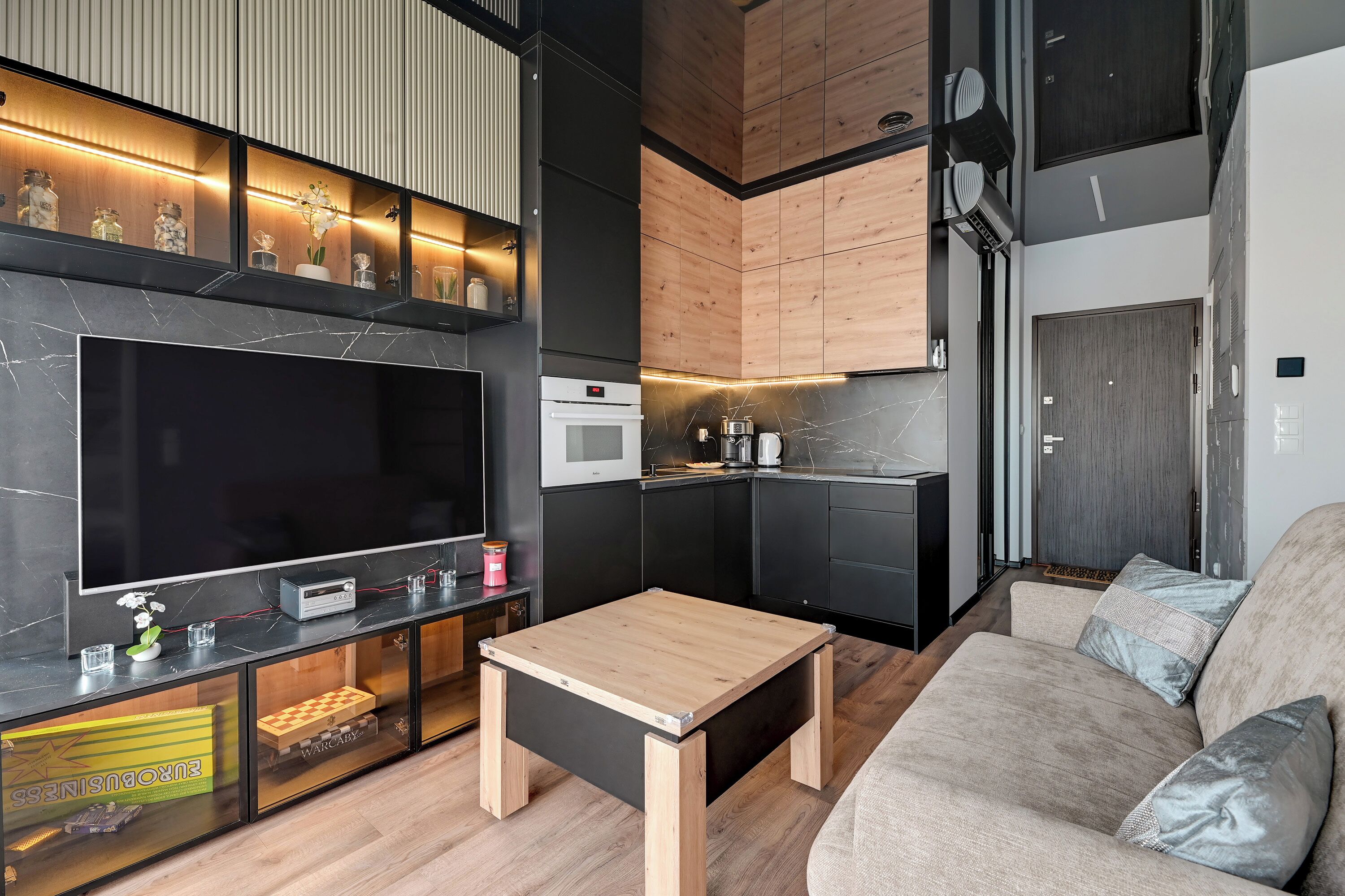 Un espacio habitable moderno con televisor de pantalla plana, armarios de madera, zona de cocina y sofá.