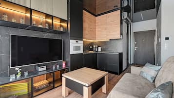 Un espacio habitable moderno con televisor de pantalla plana, armarios de madera, zona de cocina y sofá.