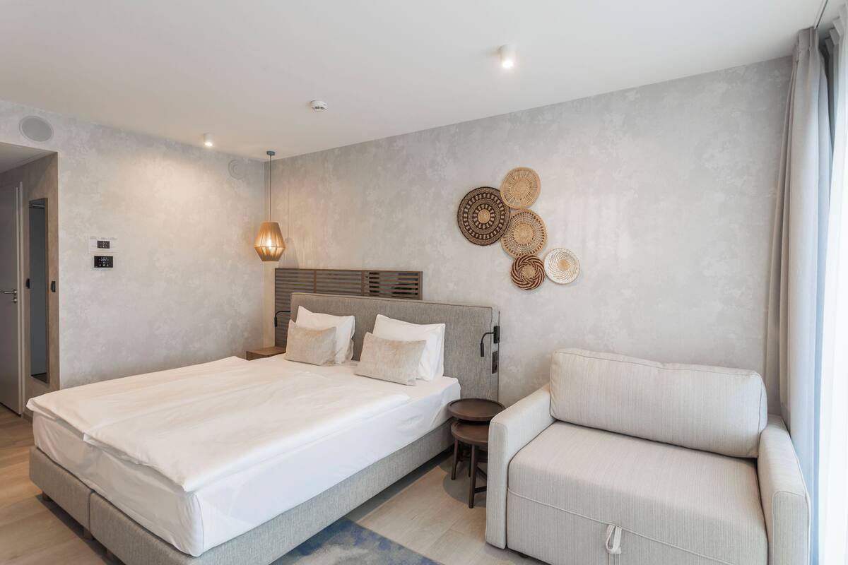 Una habitación de hotel moderna con una cama grande, un sofá, una mesita y decoración en la pared.