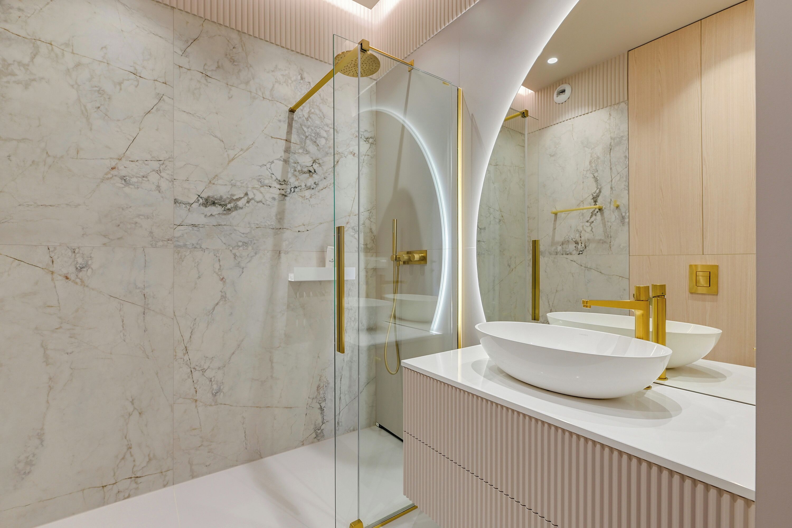 Un baño moderno con ducha de vidrio, un lavamanos blanco y un espejo grande.