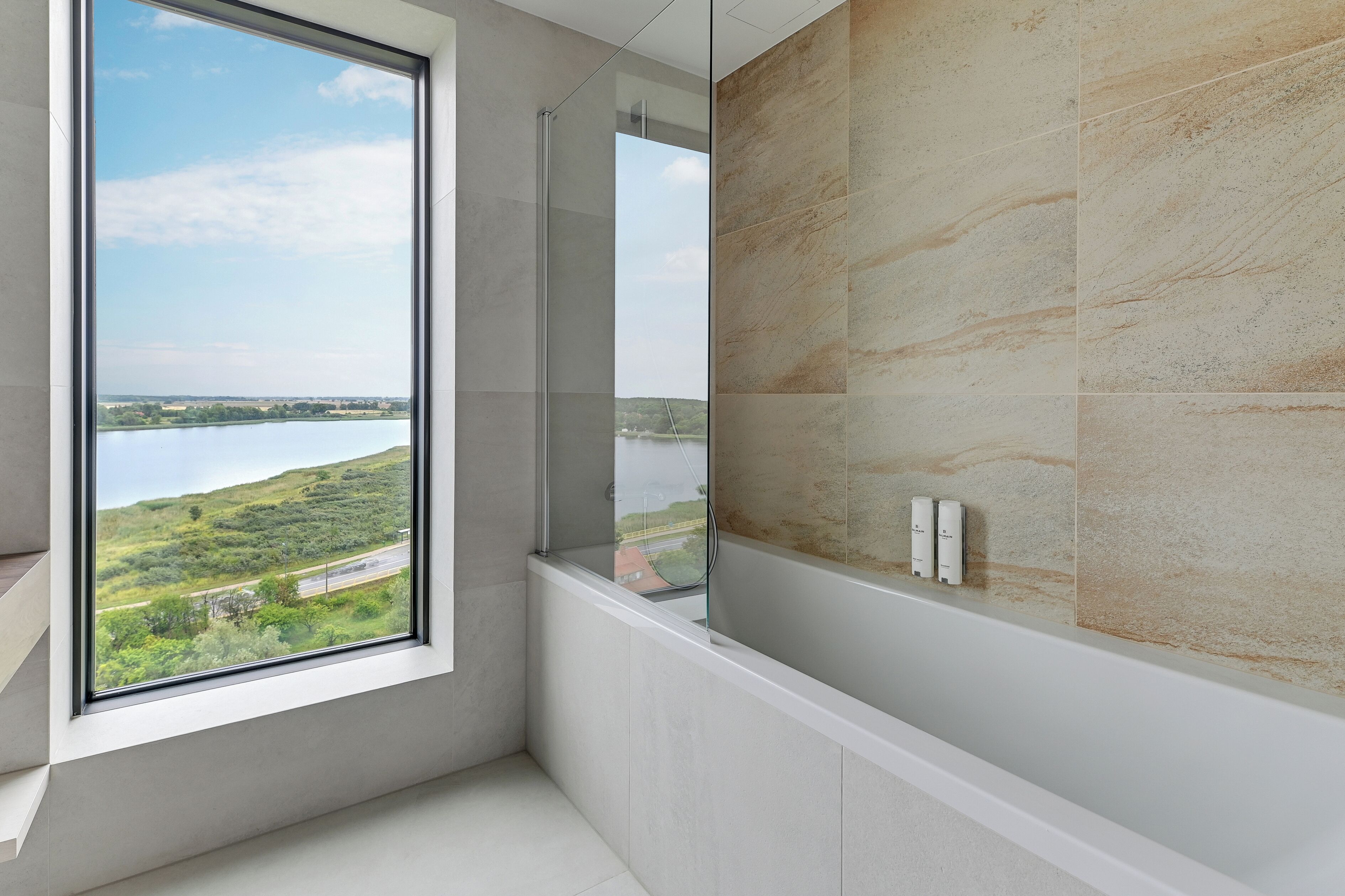 Une salle de bain dotée d’une grande fenêtre, d’une baignoire et offrant une vue sur un lac et des collines.