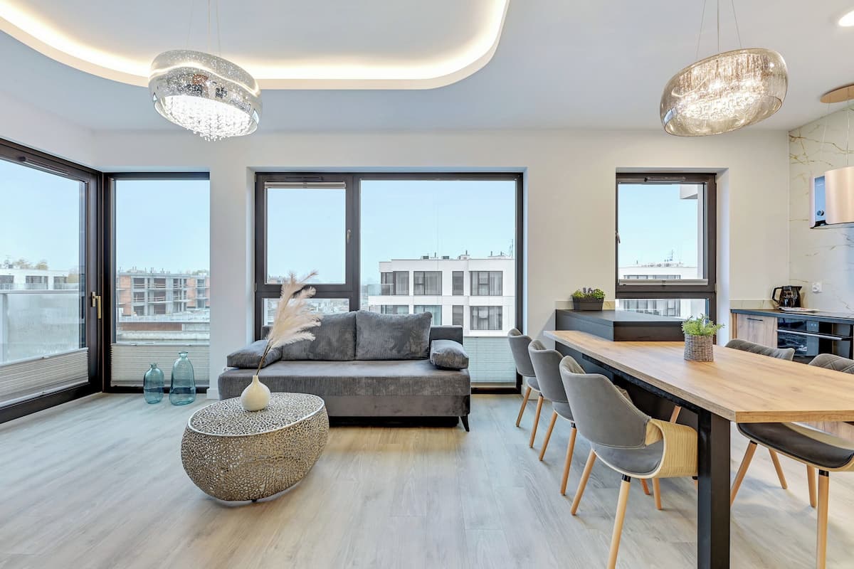 Una sala de estar moderna con un sofá, una mesa de comedor, sillas y grandes ventanales que ofrecen vistas de la ciudad.