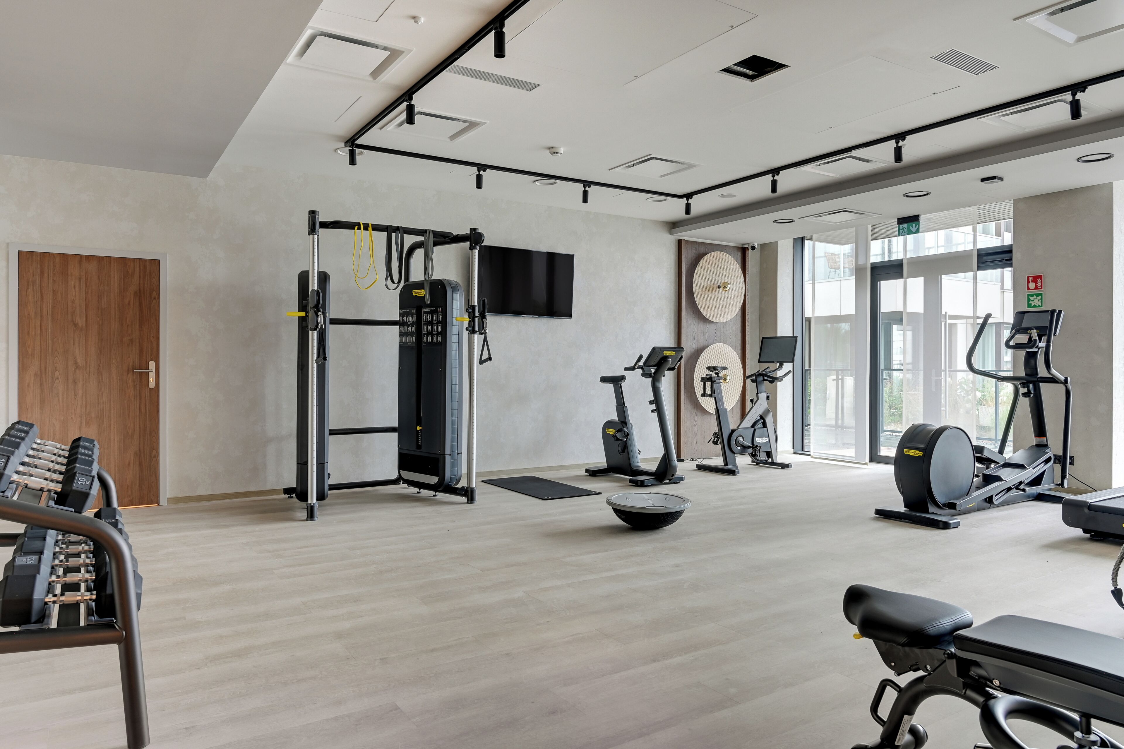 Un gimnasio moderno con diversos equipos de ejercicio, un ventanal grande y un televisor de pantalla plana.