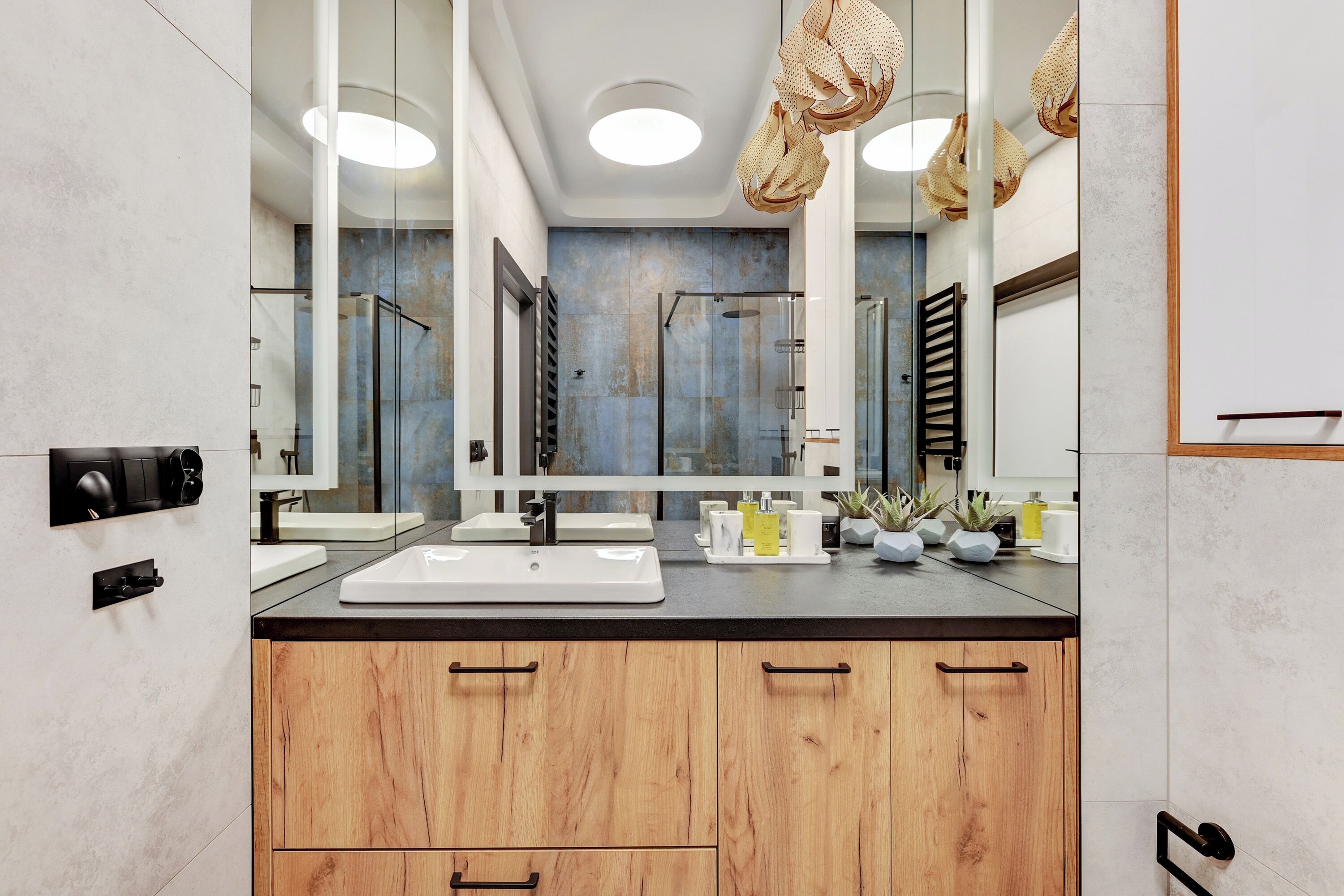 Une salle de bain moderne avec un grand miroir, deux vasques, des meubles en bois et une cabine de douche en verre.