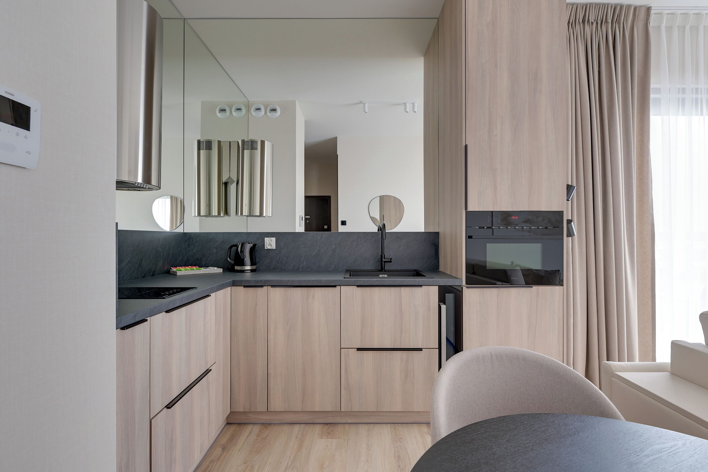 Una cocina moderna con horno integrado, cafetera y microondas. Hay una zona de comedor con mesa y sillas.