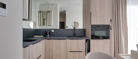 Una cocina moderna con horno integrado, cafetera y microondas. Hay una zona de comedor con mesa y sillas.