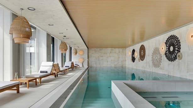 Een modern binnenzwembad met loungebedden en zonnelampen.