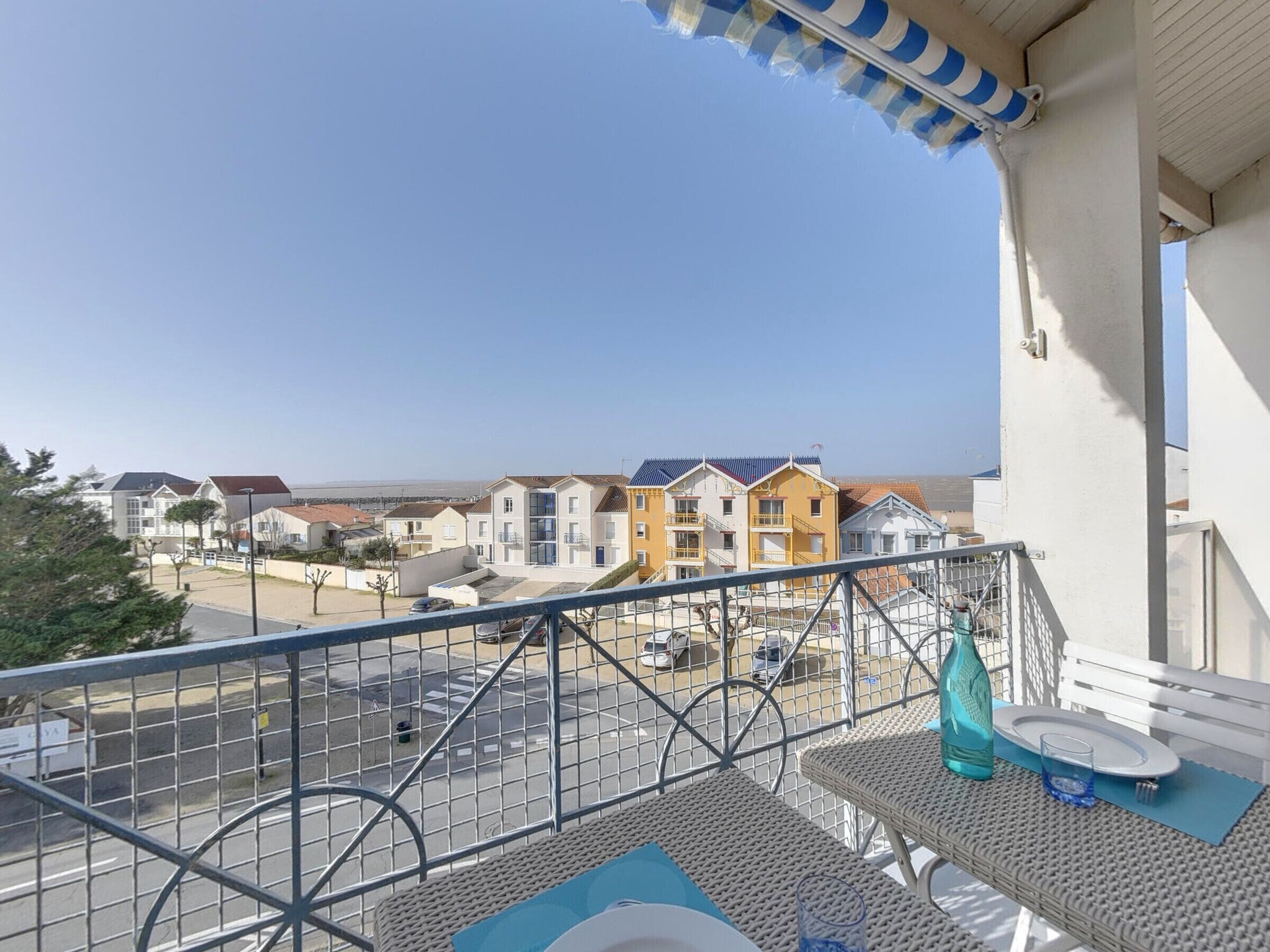 Un balcon donnant sur une ville côtière, avec une rambarde en métal et des meubles d’extérieur.