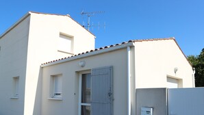 Un edificio de una sola planta con fachada blanca, techo de tejas y una antena de metal.