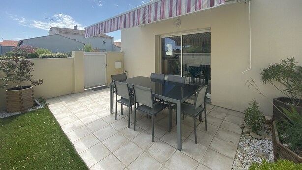 Un patio con mesa y sillas, un ventanal corredero y una pequeña área de jardín con plantas.
