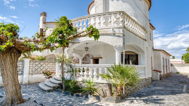Un edificio blanco con fachada de piedra, un balcón y una escalera que conduce a la entrada.