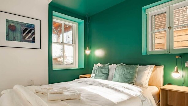 A bedroom with a bed, two bedside tables, a window, and a wall-mounted light fixture.