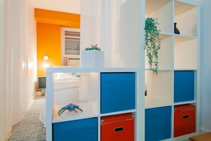 A room with a white and orange wall, a white cabinet with blue and red drawers, and a hanging plant.