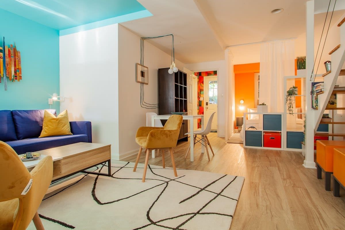 Un salón moderno con un sofá azul, cojines amarillos, una mesa de centro de madera y una alfombra estampada.