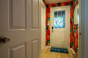A hallway with a white door, a colorful wall, and a blue doormat.