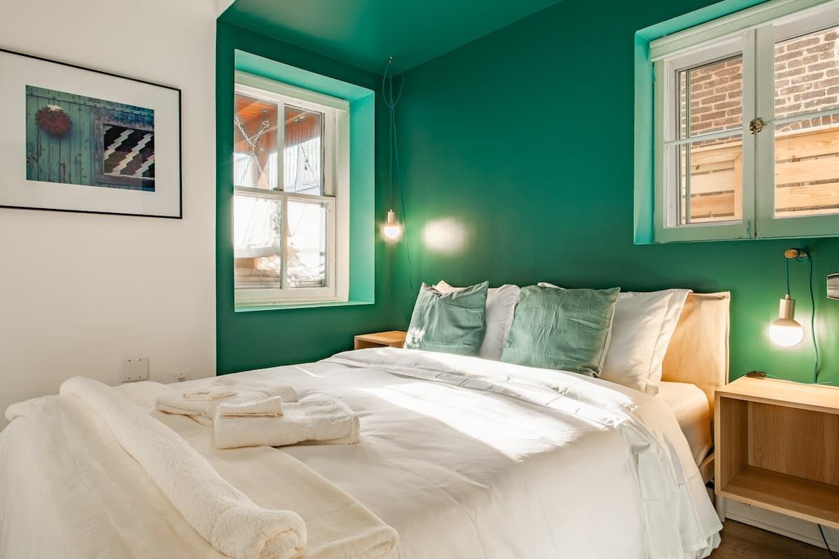 A bedroom with a bed, two bedside tables, a window, and a wall-mounted light fixture.