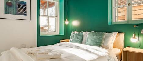 A bedroom with a bed, two bedside tables, a window, and a wall-mounted light fixture.