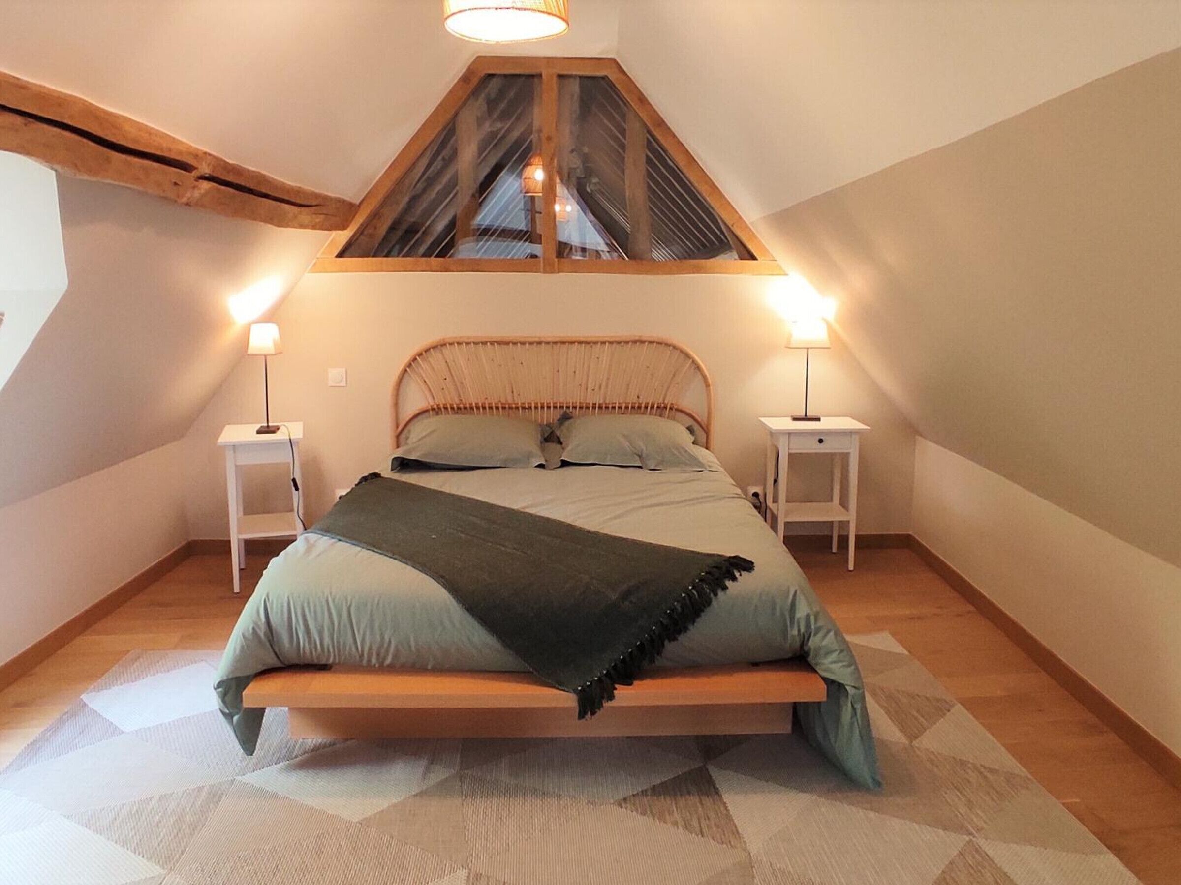 A bedroom with a sloped ceiling, a bed with a wooden headboard, two bedside tables with lamps, and a geometric patterned rug.