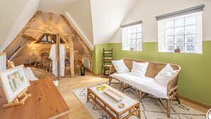 Ein gemütliches Schlafzimmer im Loft-Stil mit schrägen Wänden, einer Korbschaukel, einem Holztisch und Blick ins Freie durch ein Fenster.
