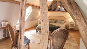 Ein Schlafzimmer im Loft-Stil mit schrägem Dach, einem Bett mit Kissen, einem Sessel, einem Schreibtisch mit Stuhl und einem Fenster.