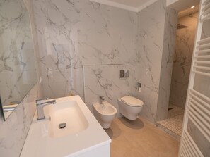 Un baño moderno con salpicadero de mármol, lavabo, bidé e inodoro.