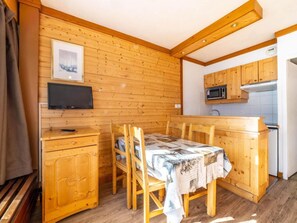 Interior de una cabaña de madera con mesa de comedor, sillas, televisor y una kitchenette.