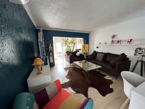 A modern living room with a blue accent wall, a brown sofa, a colorful armchair, and a glass coffee table.