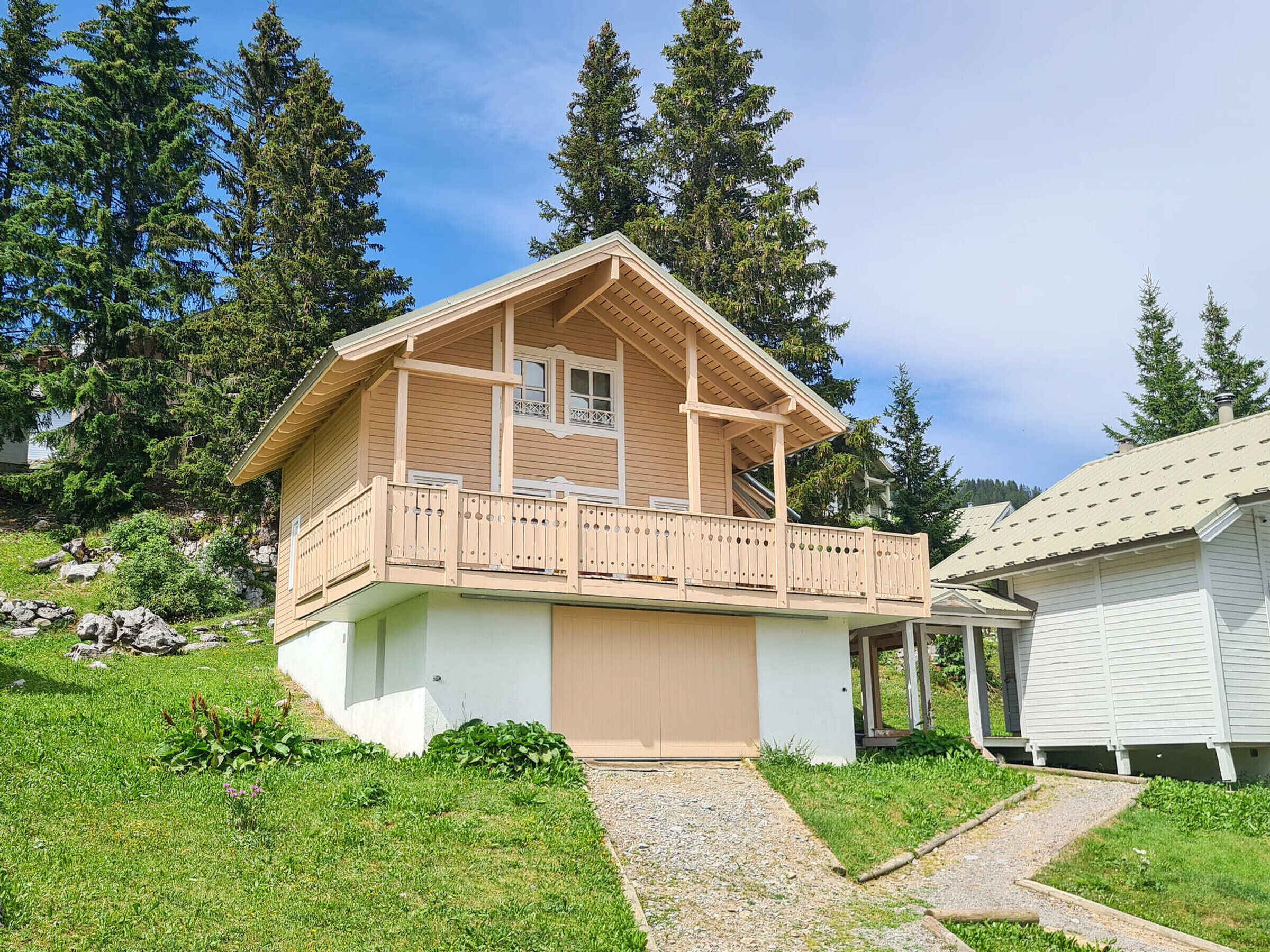 A two-story wooden cabin with a balcony, surrounded by greenery and trees.