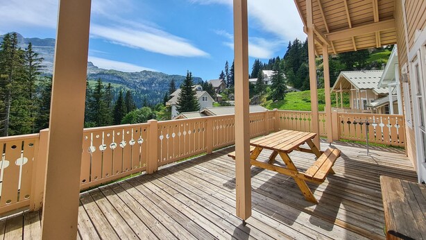 Eine Holzterrasse mit Picknicktisch und Blick auf Berge und Häuser.