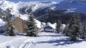 Eine verschneite Berglandschaft mit einem Chalet, das ein großes Fenster und einen Schornstein hat.