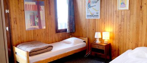 Une chambre avec un lit simple, des murs en bois, une fenêtre avec des rideaux, une lampe de chevet et une affiche accrochée au mur.