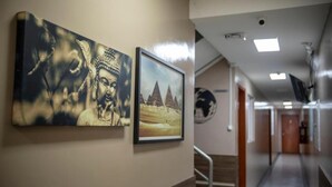 Un couloir avec deux tableaux encadrés accrochés au mur, un escalier et une porte au fond.