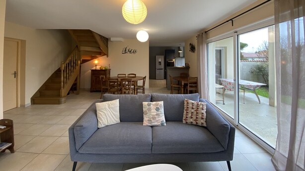 A living room with a sofa, a dining table, and a staircase. - Spacious Villa in Fouras, 10 mins from Beach, Sleeps 6, Modern Comforts, WiFi, Large Garden (Fouras)