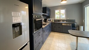 A modern kitchen with a built-in refrigerator, oven, microwave, and sink. There is a window providing natural light and a small dining table. - Spacious Villa in Fouras, 10 mins from Beach, Sleeps 6, Modern Comforts, WiFi, Large Garden (Fouras)
